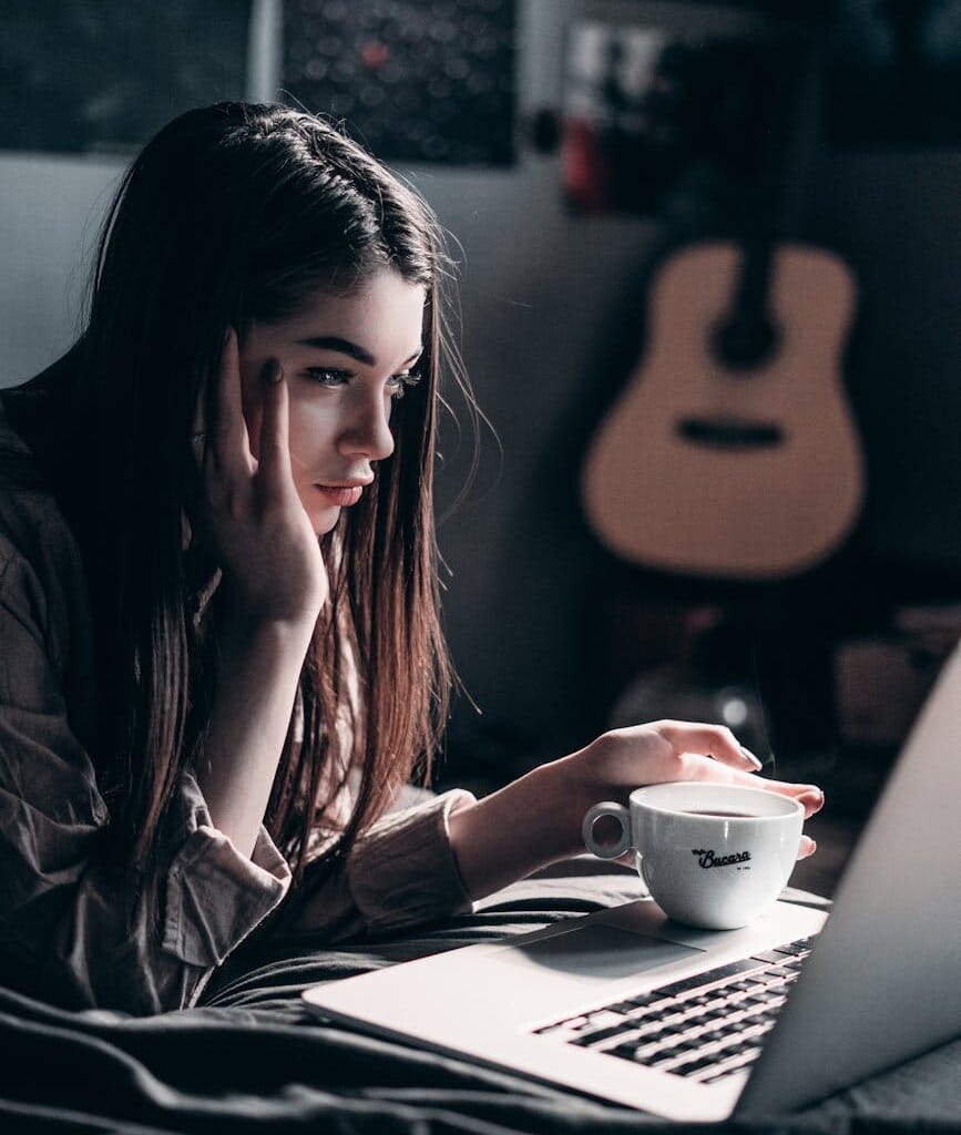 photo of woman lying on bed while using laptop