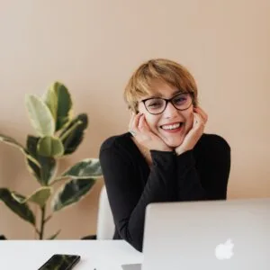 cheerful woman smiling while sitting at table with laptop