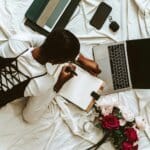 a woman laying on a bed with a laptop and flowers
